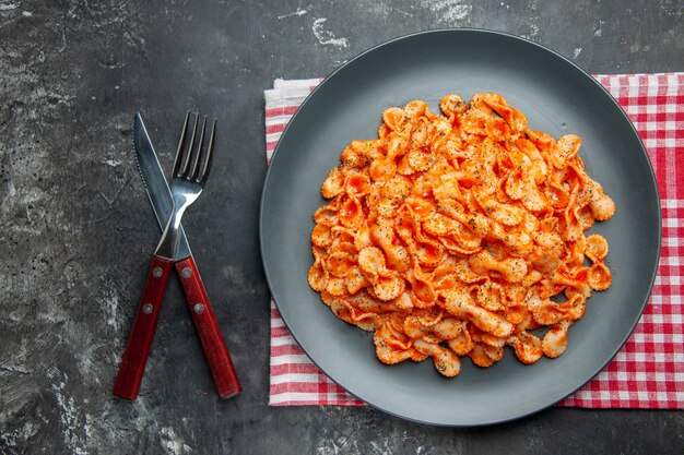 Sopra la vista di un facile pasto di pasta per cena su un piatto nero e posate su un asciugamano spogliato rosso su uno sfondo scuro