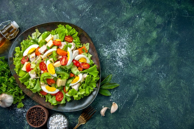 Sopra la vista di una deliziosa insalata fatta in casa con molti ingredienti in un piatto e spezie caduti sulla forcella della bottiglia di olio sul tavolo dei colori della miscela verde nero con spazio libero