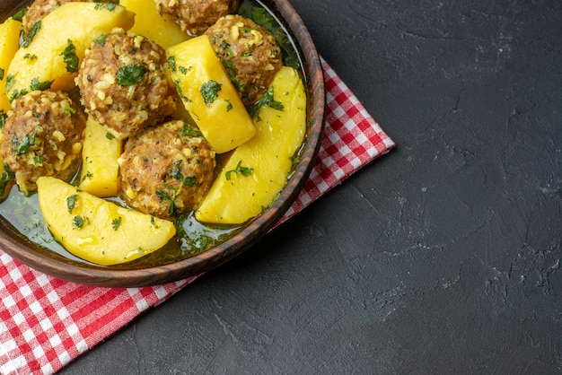 Sopra la vista di una gustosa cena con polpette di patate verdi in una ciotola marrone su asciugamano rosso su sfondo nero con spazio libero