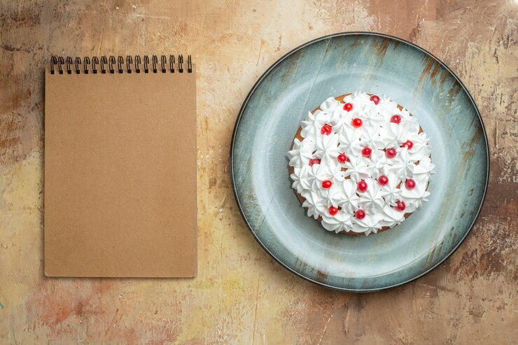 Foto gratuito sopra la vista di una gustosa torta decorata con crema e ribes su un piatto blu e un quaderno a spirale su un tavolo colorato