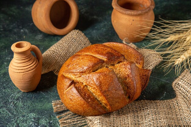 Sopra la vista di una pagnotta di pane nero dietetico su un asciugamano marrone e ceramiche sulla superficie di colori scuri