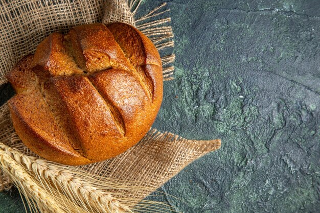 Sopra la vista di una pagnotta di pane nero dietetico su un asciugamano marrone sulla superficie di colori scuri