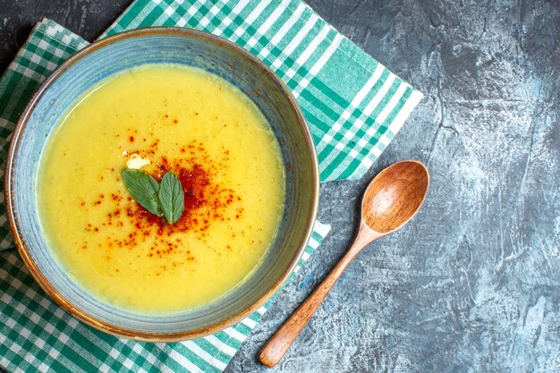 Sopra la vista di una pentola blu con una gustosa zuppa servita con menta e cucchiaio di legno su un asciugamano verde spogliato su sfondo blu