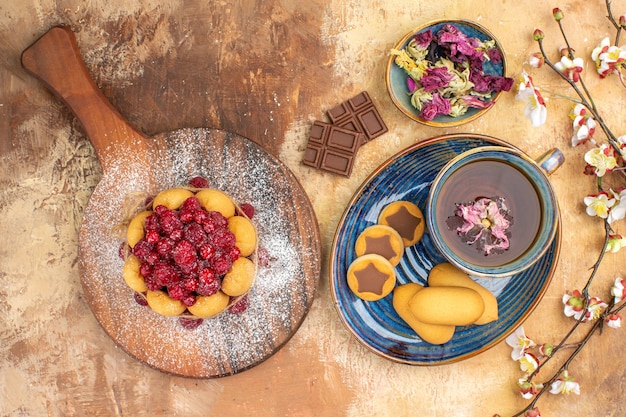 Sopra la vista di vari biscotti e torta morbida una tazza di tè e barrette di cioccolato ai fiori