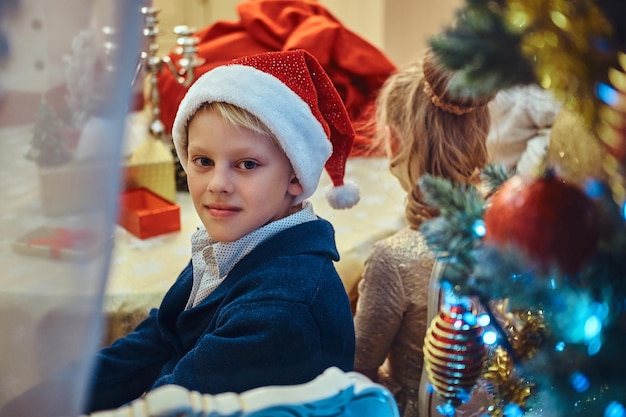 Sorella e fratello felici seduti a tavola in un elegante soggiorno decorato per Natale.