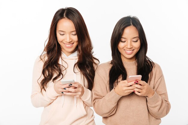Sorelle asiatiche abbastanza felici delle signore che chiacchierano dai telefoni cellulari.