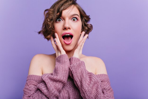 Sorpresa bella ragazza con bellissimi occhi in posa con interni viola. Foto dell'interno della giovane donna castana riccia divertendosi sul servizio fotografico.