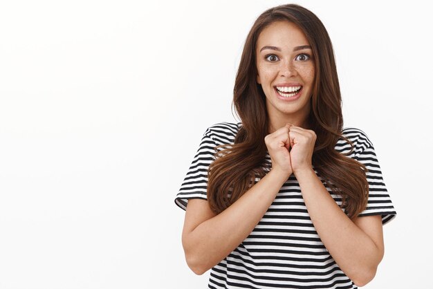 Sorpresa eccitata giovane ragazza carina stringere le mani insieme sorridente divertito non può credere che lei fortunata vincitrice trionfante sguardo con adorazione e gioia la fotocamera non vede l'ora di ricevere il premio sfondo bianco