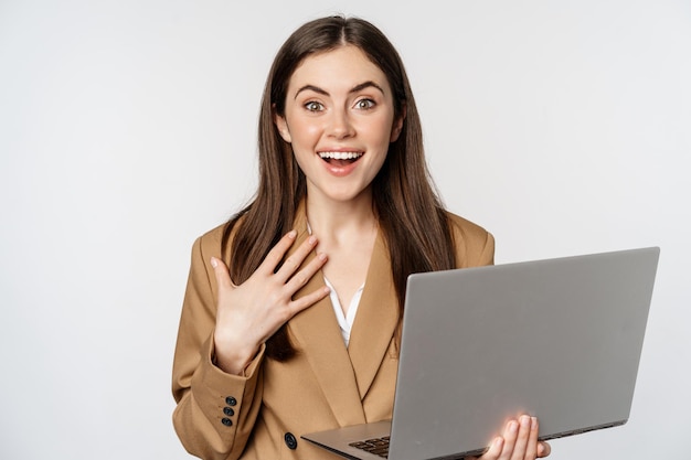 Sorpresa ed eccitata donna d'affari in possesso di laptop, reagendo stupita di smth fantastico, in piedi in tuta su sfondo bianco.