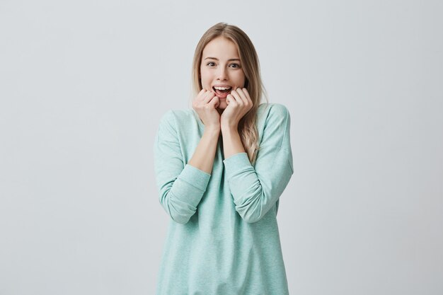 Sorpresa giovane bella femmina con lunghi capelli biondi, guarda con la bocca aperta, eccitata di vedere qualcosa di piacevole, vestita casualmente. sorpresa ed espressione facciale