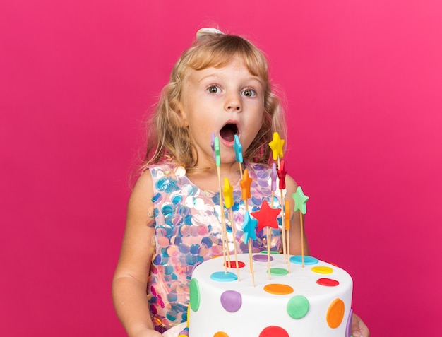 sorpresa piccola ragazza bionda che tiene la torta di compleanno isolata sulla parete rosa con lo spazio della copia