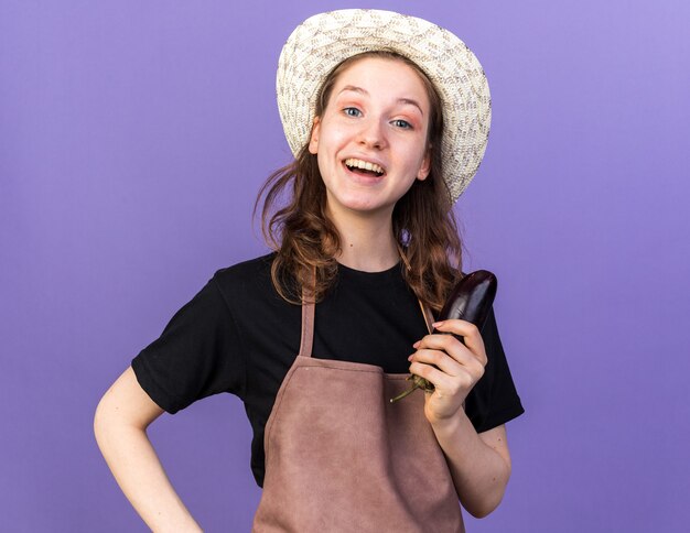 Sorpreso giovane giardiniere femminile che indossa cappello da giardinaggio che tiene melanzane