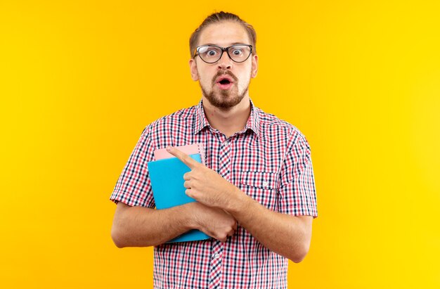 Sorpreso giovane studente che indossa uno zaino con gli occhiali che tengono i punti del libro a lato