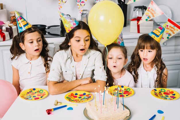 Sorpreso ragazze guardando la torta di compleanno con candele illuminate e palloncini gialli