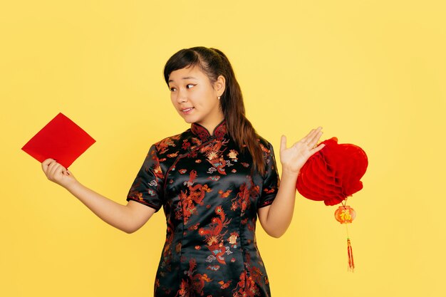 Sorridendo con lanterna e busta. Felice anno nuovo cinese 2020. Ritratto di ragazza asiatica su sfondo giallo. Il modello femminile in abiti tradizionali sembra felice. Celebrazione, emozioni. Copyspace.