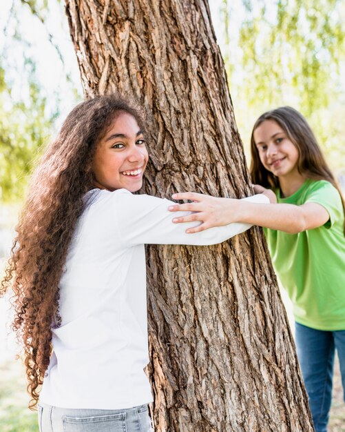 Sorridendo due ragazze che abbracciano il grande tronco d&#39;albero