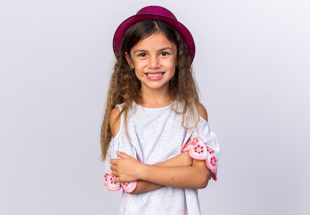 sorridente bambina caucasica con cappello da festa viola in piedi con le braccia incrociate isolato sul muro bianco con spazio di copia