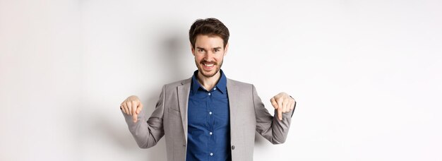 Sorridente bell'uomo in giacca e cravatta che punta le dita verso il basso mostrando un buon affare guarda qui gesto stan