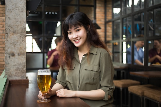 Sorridente bella donna asiatica bevendo birra nel pub
