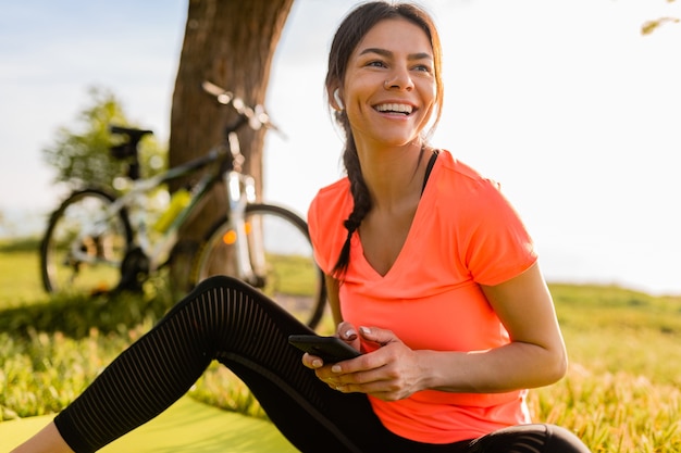 Sorridente bella donna che tiene il telefono facendo sport mattina nel parco