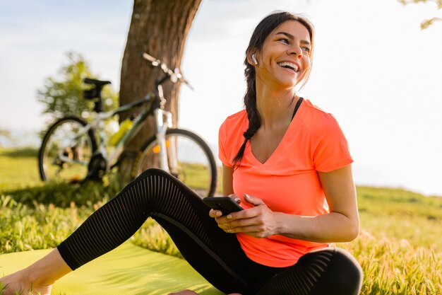 Sorridente bella donna che tiene il telefono facendo sport mattina nel parco