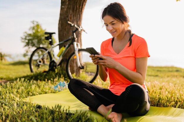 Sorridente bella donna che tiene il telefono facendo sport mattina nella natura del parco