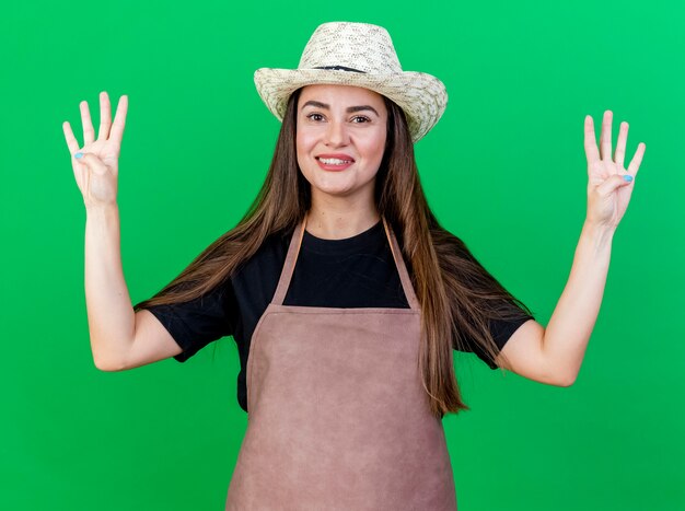 Sorridente bella ragazza giardiniere in uniforme che indossa il cappello da giardinaggio che mostra quattro isolati su sfondo verde