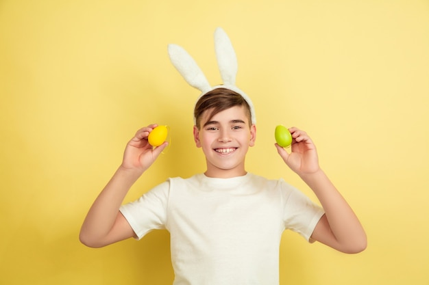 Sorridente. Caccia alle uova in arrivo. Ragazzo caucasico come un coniglietto di Pasqua su sfondo giallo studio. Auguri di buona Pasqua. Bellissimo modello maschile. Concetto di emozioni umane, espressione facciale, vacanze. Copyspace.