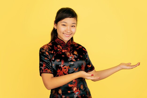 Sorridente carino, mostrando a lato. Buon Capodanno cinese. Ritratto di ragazza asiatica su sfondo giallo. Il modello femminile in abiti tradizionali sembra felice. Celebrazione, emozioni umane. Copyspace.