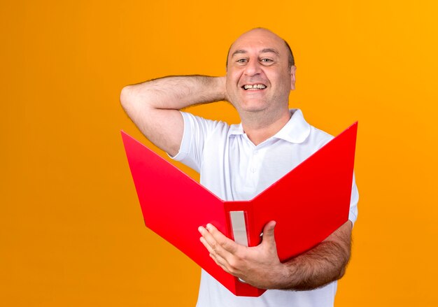 Sorridente casual uomo maturo tenendo la cartella e mettendo la mano dietro la testa isolata su colore giallo