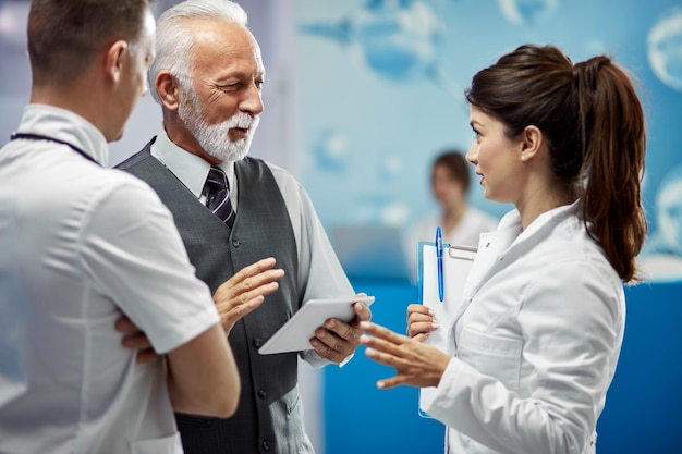 Sorridente consulente finanziario maturo e medici che comunicano stando in piedi in una lobby presso la clinica medica