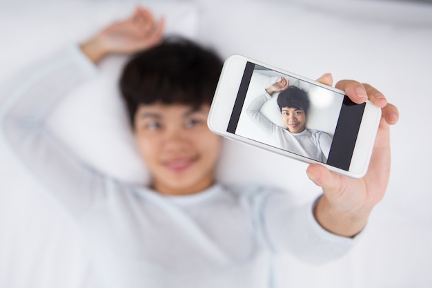 Sorridente donna abbastanza asiatica che prende Selfie nel letto