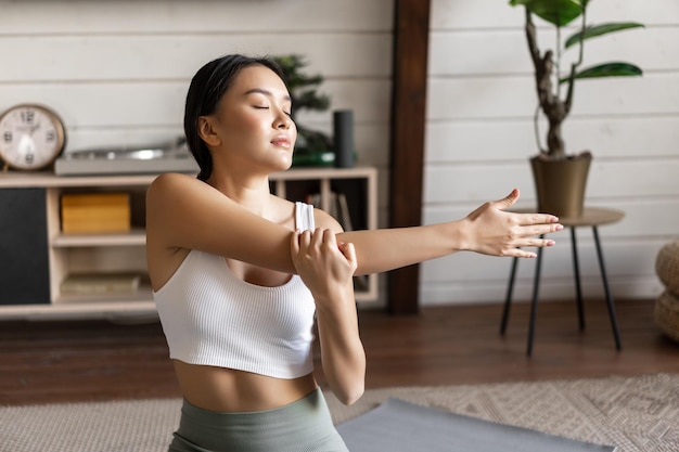 Sorridente donna asiatica che fa stretching allenamento fitness a casa in soggiorno indossando abbigliamento sportivo