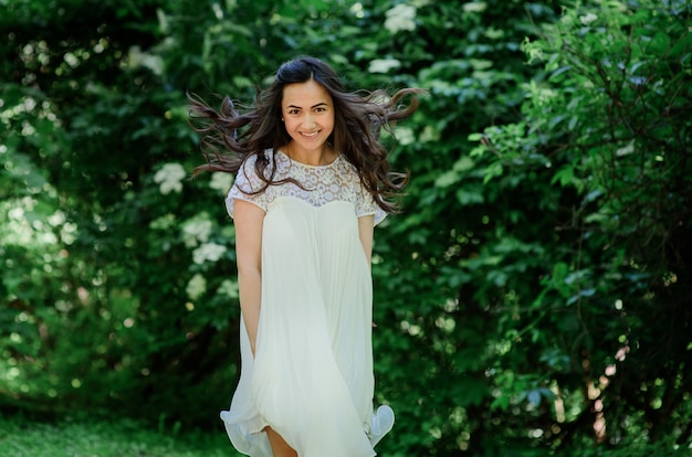 Sorridente donna bruna in abito bianco pone in giardino