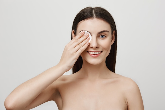 Sorridente donna carina trucco di decollo con un batuffolo di cotone