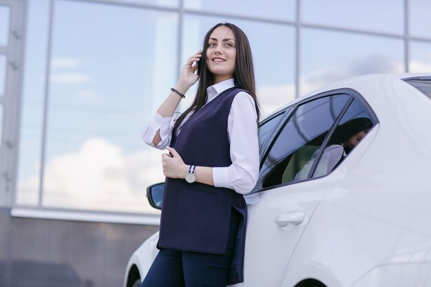 Sorridente donna che parla al telefono appoggiato su una macchina