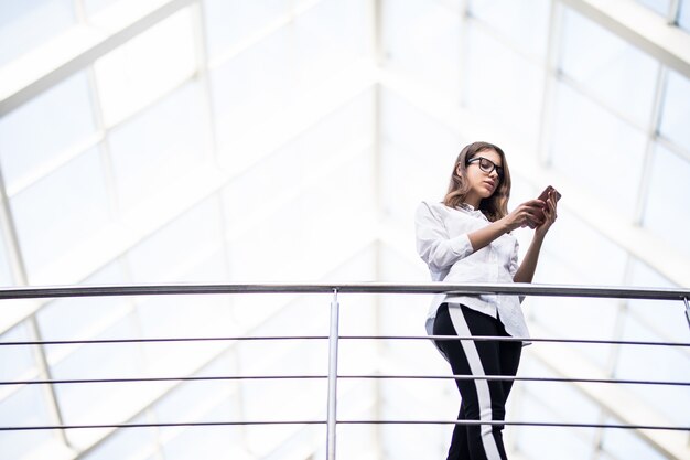 Sorridente donna d'affari di successo donne in piedi a riposo e guardando attraverso sul balcone nel moderno centro ufficio vestito in t-shirt bianca