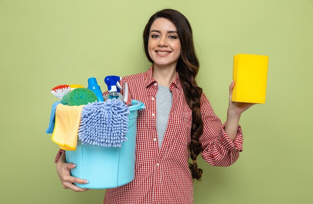 Sorridente donna delle pulizie piuttosto caucasica che tiene in mano attrezzatura per la pulizia e spugna