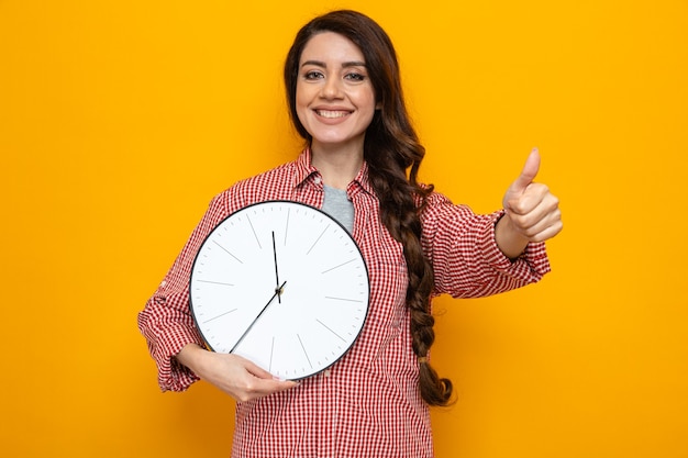 Sorridente donna delle pulizie piuttosto caucasica che tiene l'orologio e fa il pollice in su