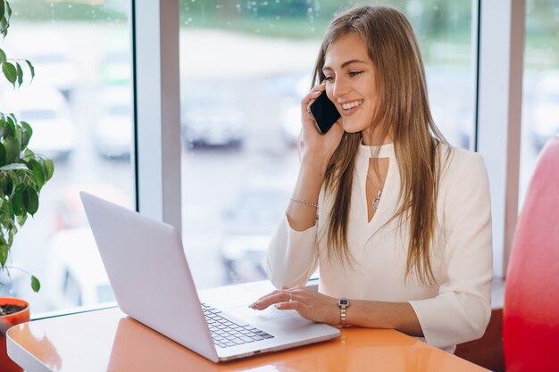 Sorridente donna elegante parla al telefono e lo schermo del suo computer