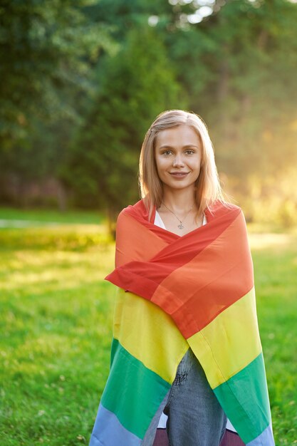 Sorridente donna tollerante che tiene bandiera lgbt all'aperto