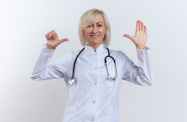 Sorridente dottoressa adulta slava in veste medica con stetoscopio che punta alla sua mano isolata su sfondo bianco con spazio copia