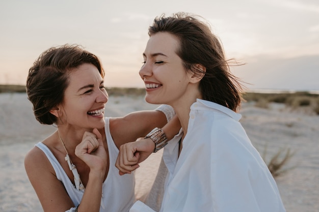 Sorridente due giovani donne amici divertendosi sulla spiaggia al tramonto, romanticismo gay amore lesbico