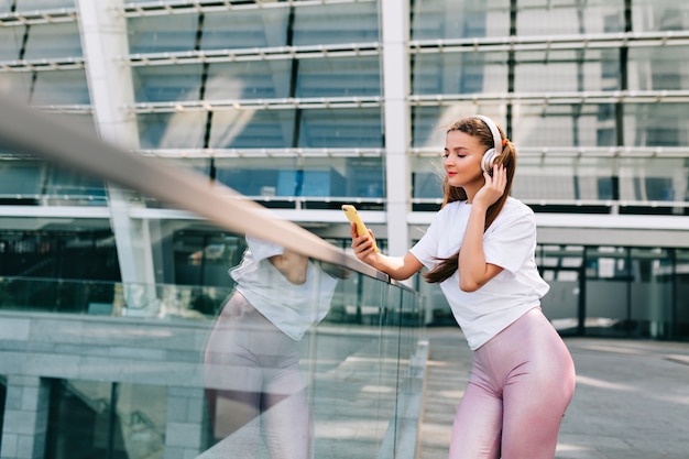 Sorridente e danza giovane donna che tiene uno smartphone e ascolta musica in cuffia