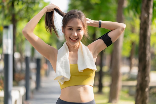 Sorridente femmina asiatica sport attivo stile di vita riscaldamento stretching prima di eseguire esercizio mentre si sistemano i capelli nel parco allenamento mattutino stile di vita sano benessere vita