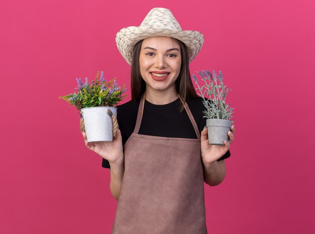 Sorridente giardiniere femmina caucasica che indossa un cappello da giardinaggio che tiene vasi da fiori