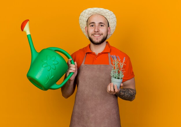 Sorridente giardiniere uomo che indossa un cappello da giardinaggio tiene annaffiatoio e pianta in vaso di fiori