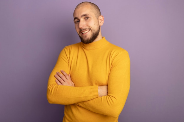 Sorridente giovane bel ragazzo attraversando le mani isolate sulla parete viola con lo spazio della copia