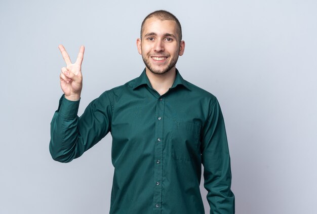 Sorridente giovane bel ragazzo che indossa una camicia verde che mostra gesto di pace