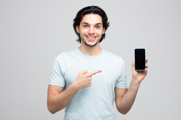 sorridente giovane bell'uomo guardando la fotocamera che mostra il telefono cellulare che punta ad esso isolato su sfondo bianco